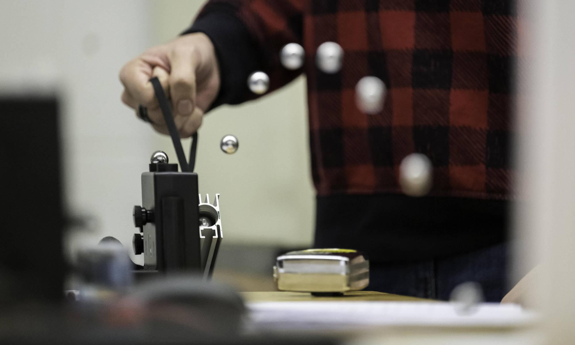 Composite photo of a metal ball shot through a spring-loaded launcher during mechanical engineering class and lab.